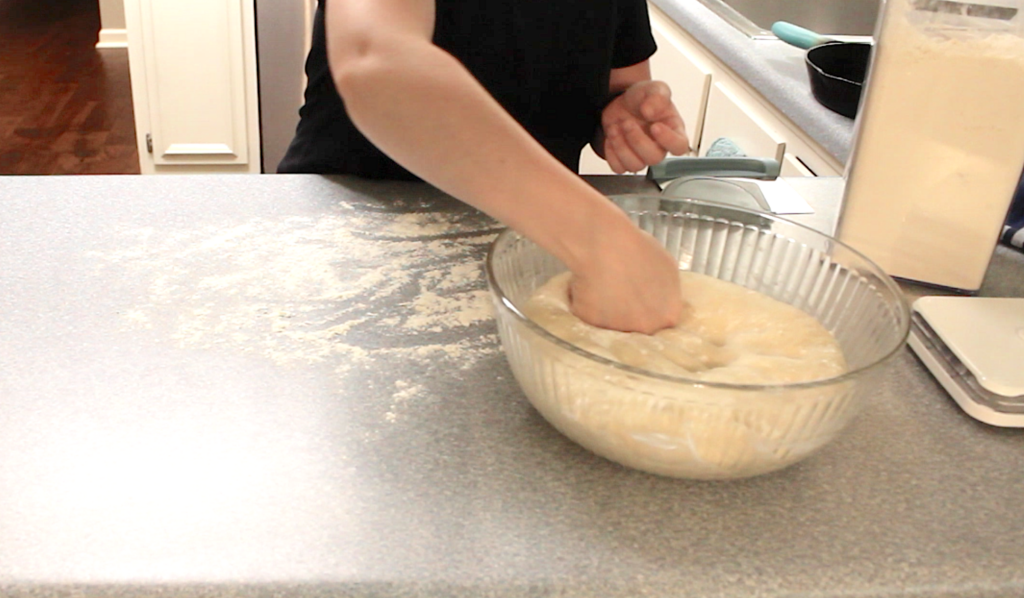 punching dough down in a glass bowl