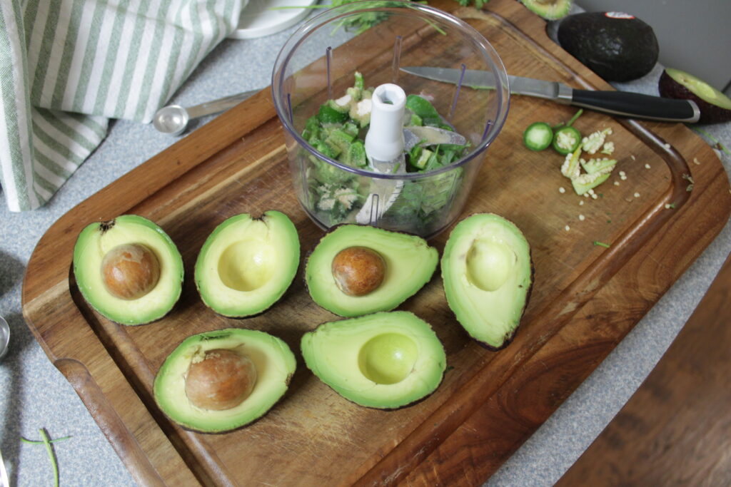 food processor, 6 halves of avocados sitting on wooden cutting board
