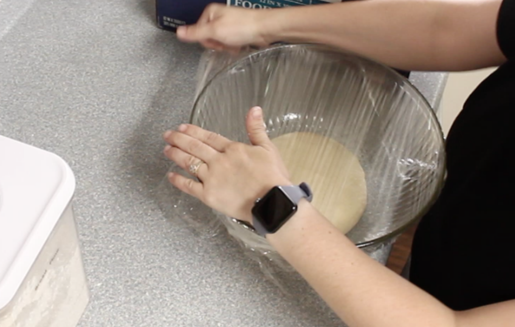 covering dough in glass bowl with plastic wrap