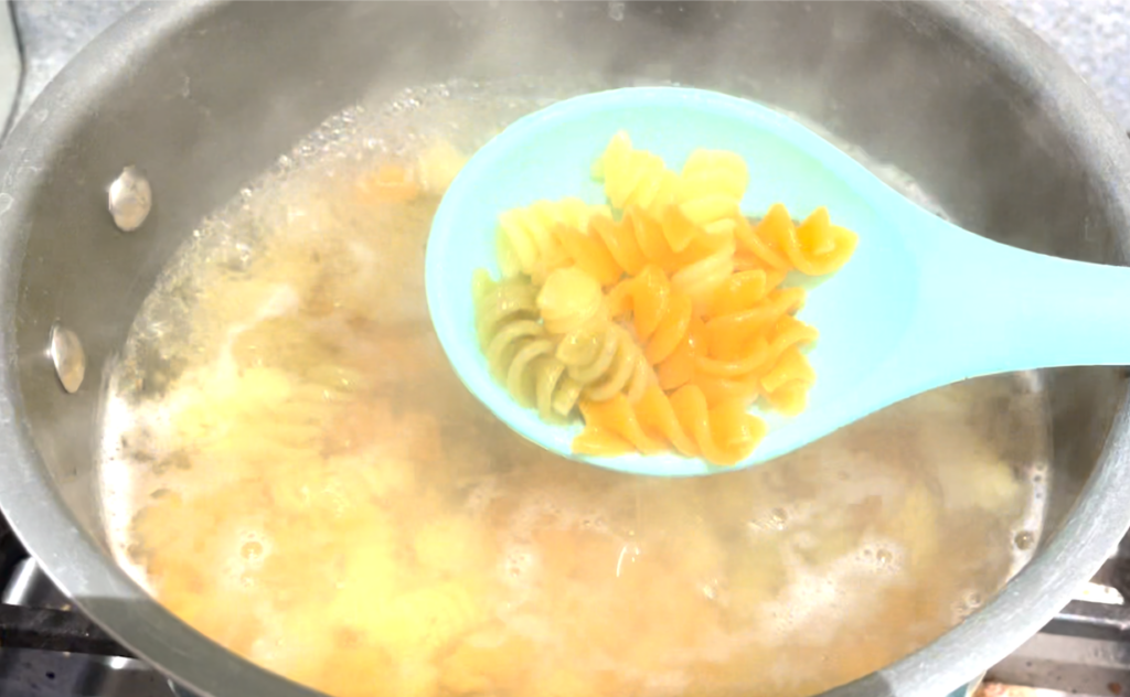 boiling tricolor rotini pasta, spoon full of pasta over boiling pot 